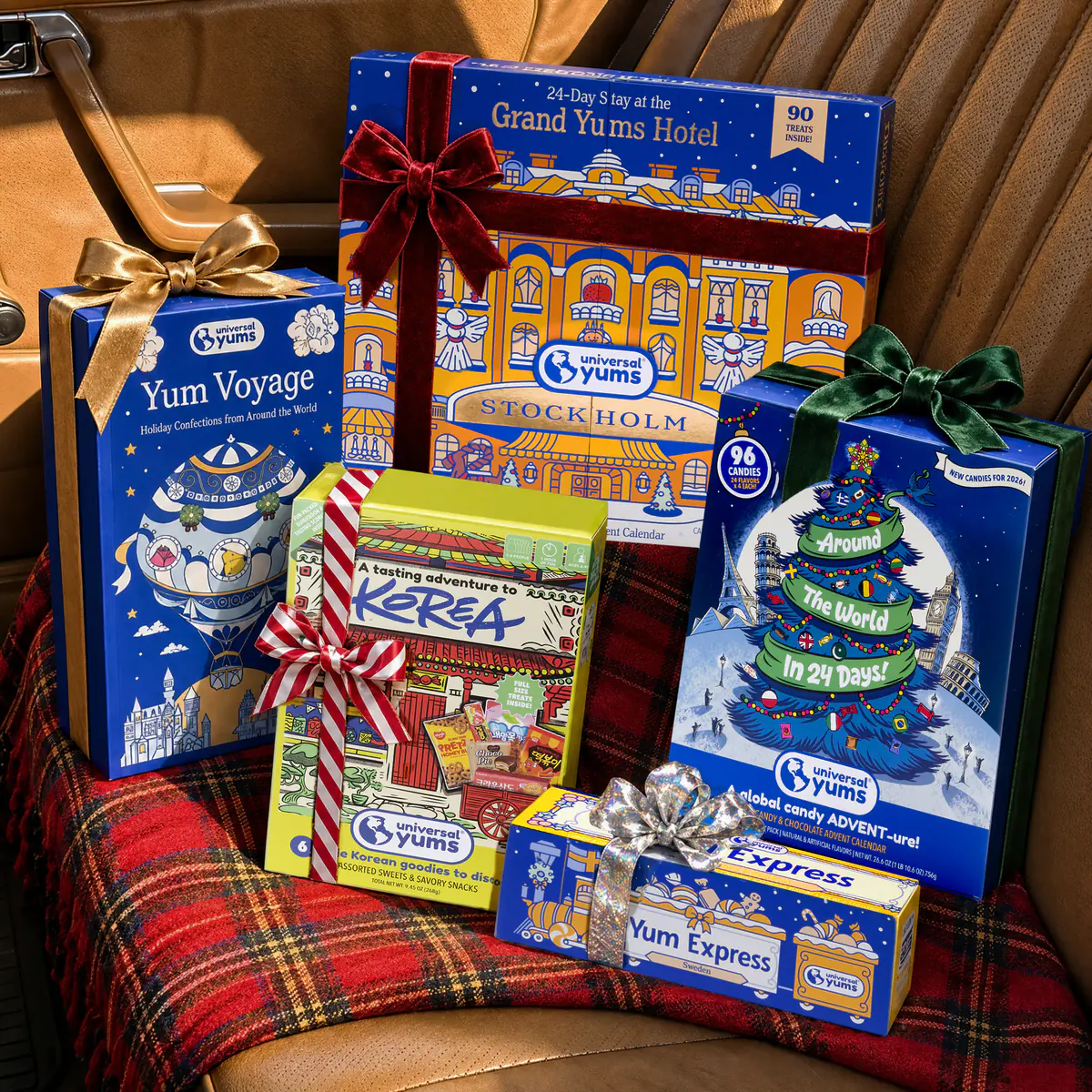 Universal Yums holiday gift boxes tied with bows, stacked on a plaid blanket on a leather car seat.